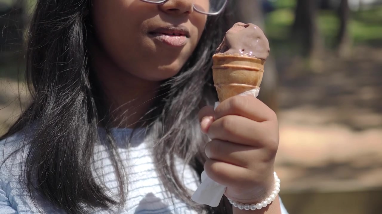 Jovem menina saboreando um sorvete de chocolate ao ar livre