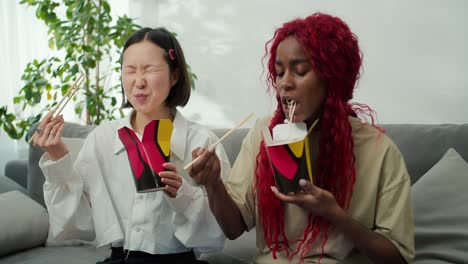 diversas amigas comiendo fideos juntas en casa usando palillos