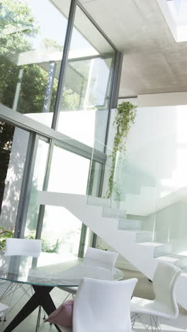 vertical video: modern home interior with glass walls, white staircase, and dining area