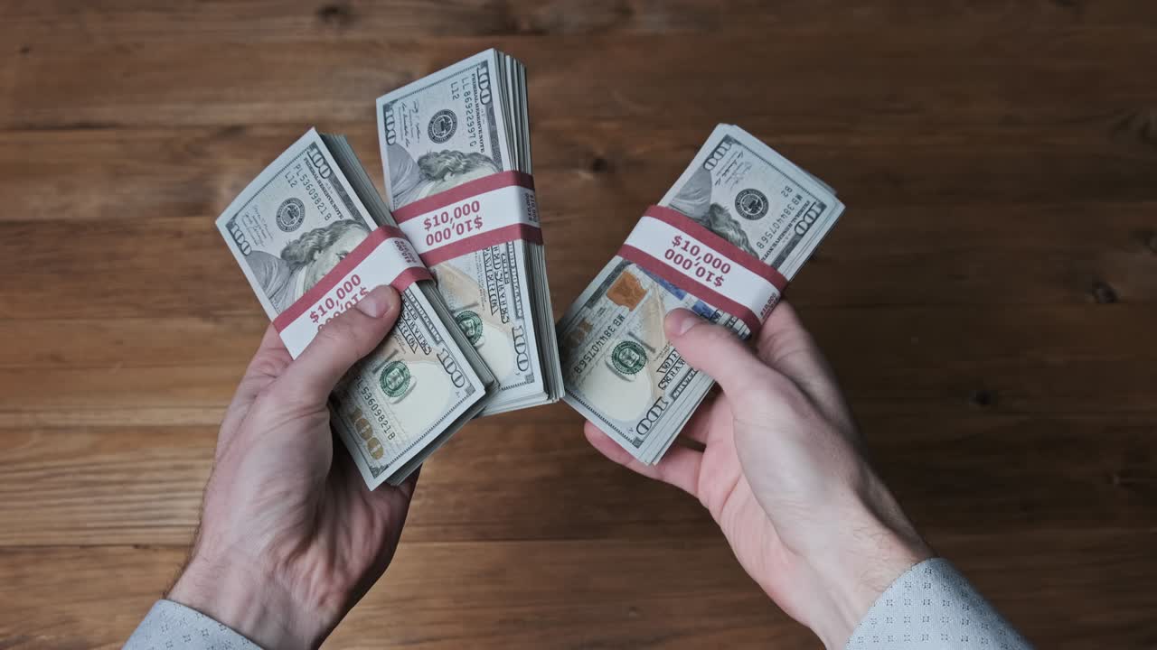 las manos masculinas sostienen tres pilas de billetes de 10.000 dólares estadounidenses y muestran el pulgar hacia arriba.