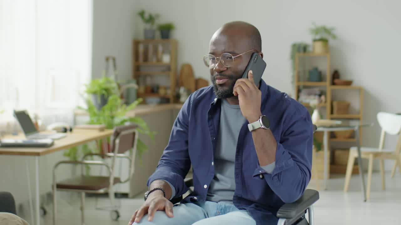 Homme noir en fauteuil roulant parlant au téléphone chez lui