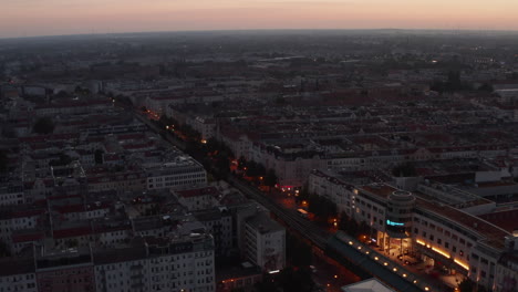 Pan-and-tilt-up-footage-of-morning-city.-Wide-street-lined-with-multistorey-tenement-houses-before-sunrise,-orange-twilight-sky.-Berlin,-Germany