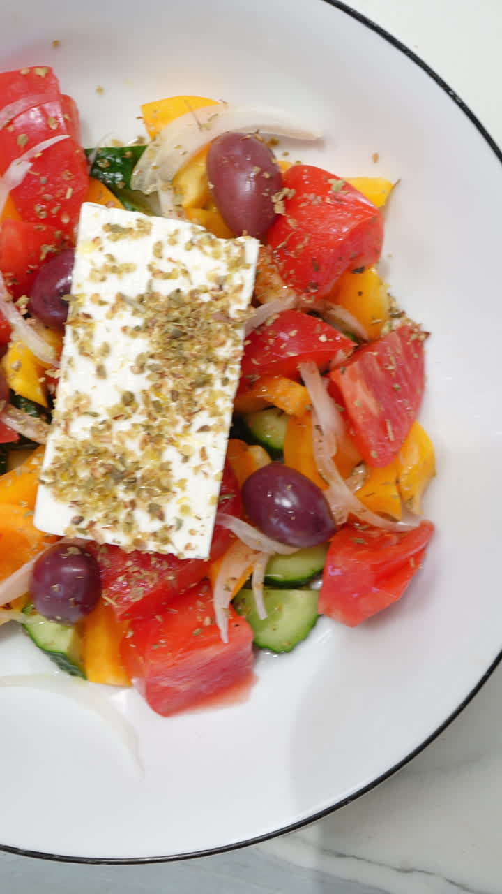 Vertical footage Greek salad ingredients layering in white bowls, progressively adding tomatoes, cucumbers, sauce, olives, feta, avocado cream, arugula, salmon, croutons, and sunflower seeds