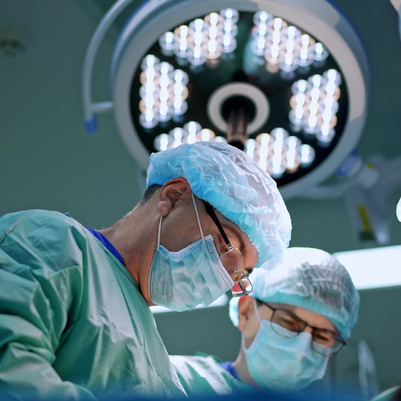 Team of doctors bent over the patient in surgery room. Low angle view on the surgeons from patient's perspective
