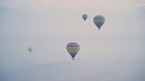 Grupo-De-Globos-Aerostáticos-Vuelan-Sobre-El-Paisaje-Brumoso-De-Marruecos,-Vista-De-Mano