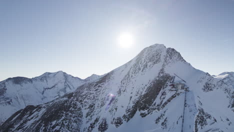 aerial drone footage of majestic snowy mountain peaks at sunrise, revealing an enchanting alpine landscape and the rising sun's radiant glow