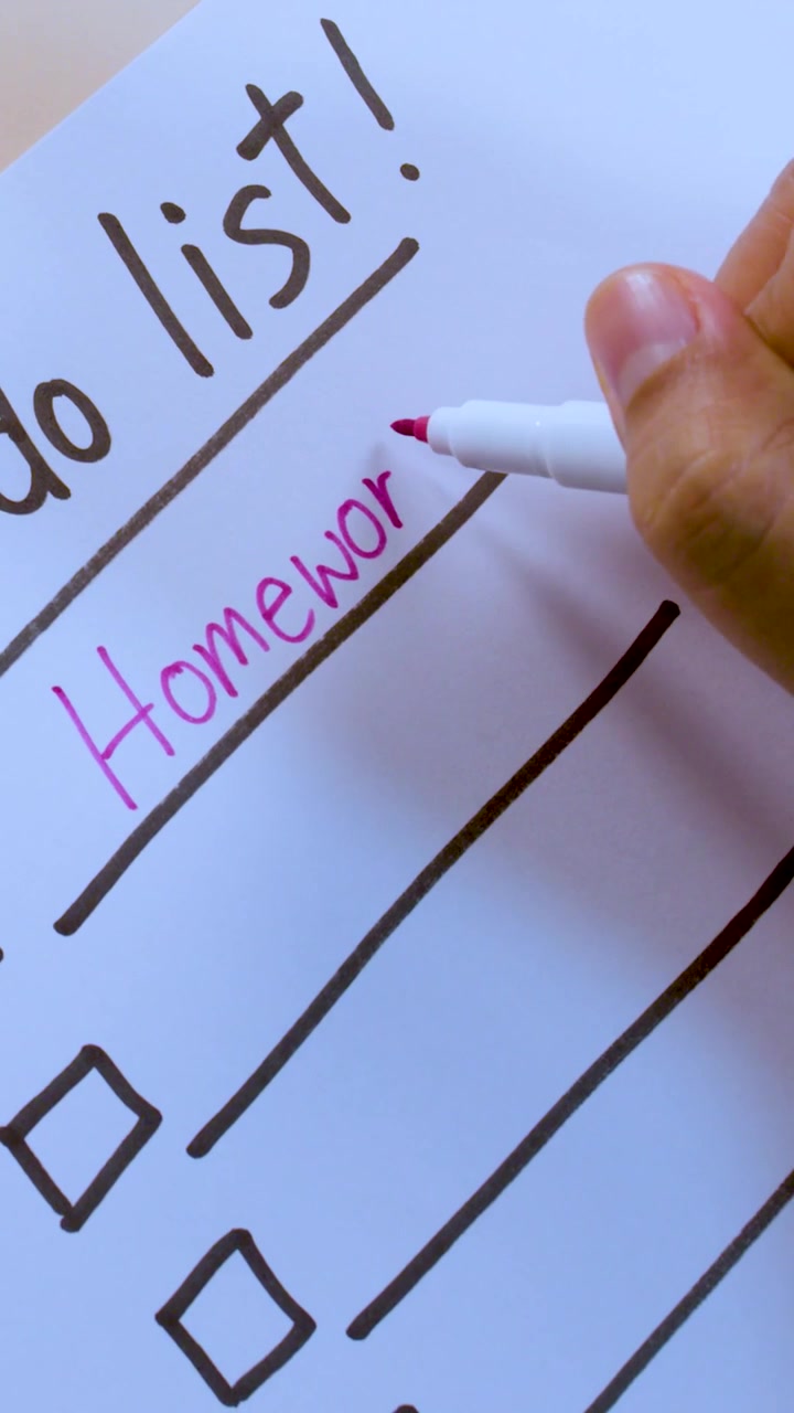 Mano che scrive "Compiti" su una lista di cose da fare con un pennarello rosa