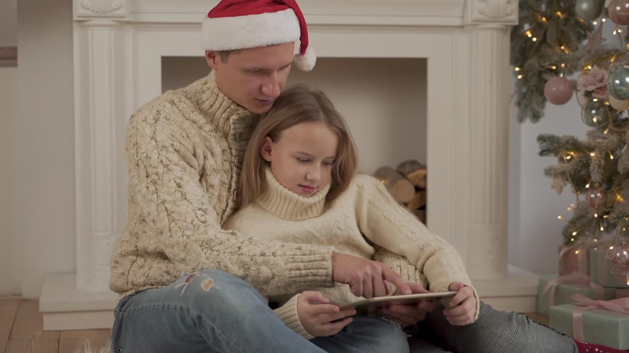 padre e hija jugando con una tableta en navidad con un sombrero de santa