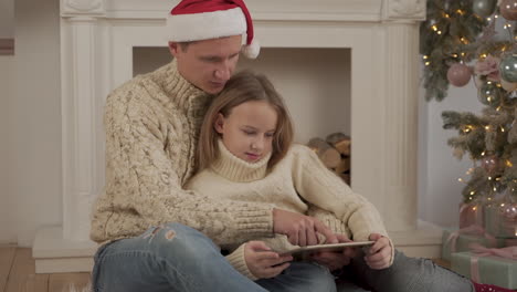 father and daughter playing with a tablet at christmas wearing a santa's hat