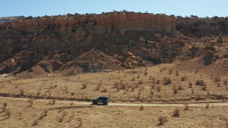 aerial following car on desert road with large rock formation in background