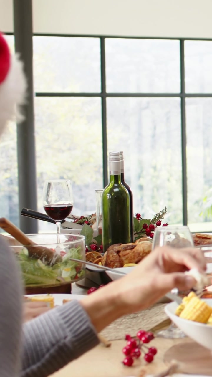 Vertical video: Reaching elder in Santa hat, gray sweater picking corn to eat near wine, copy space