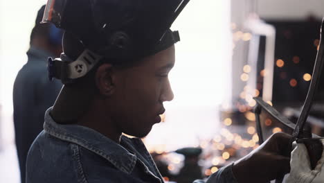 young black male profile working on steel structure in workshop with sparks bokeh slow motion