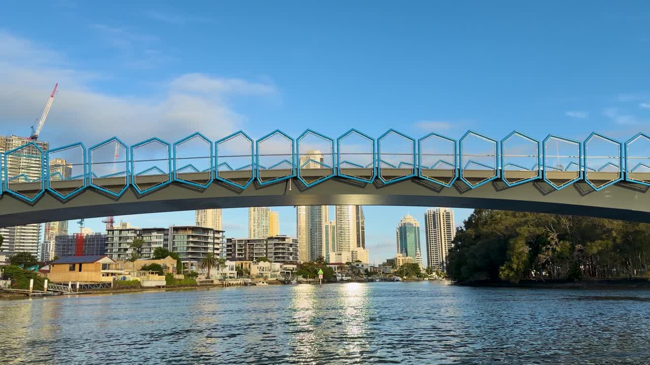 Boat glides under Chevron Island bridge, revealing Gold Coast skyline, calm river, golden hour lighting