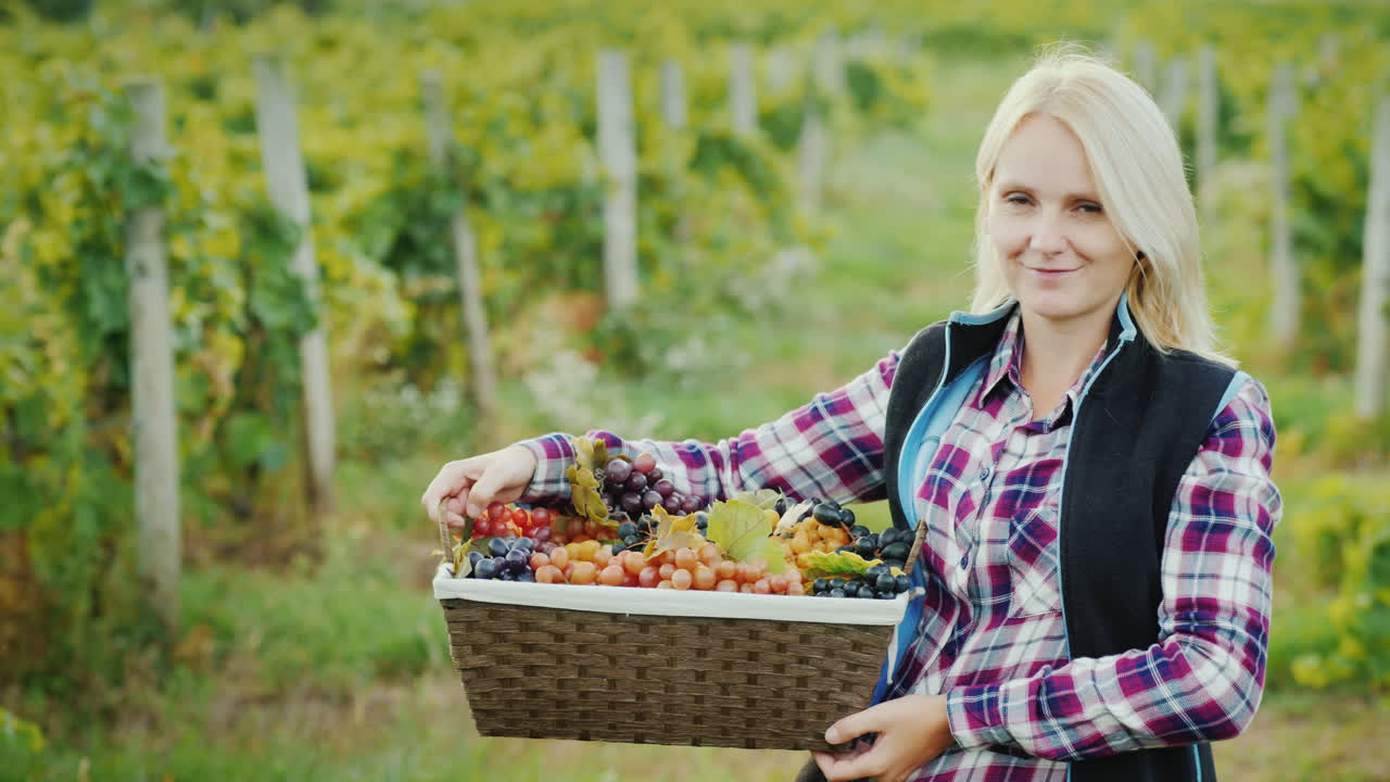 포도 미소가 담긴 바구니를 든 매력적인 농부의 초상화가 카메라를 쳐다본다