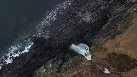 birdseye over a rocky cliff with a waterfall going into the atlantic ocean at kilt rock isle of skye, scotland