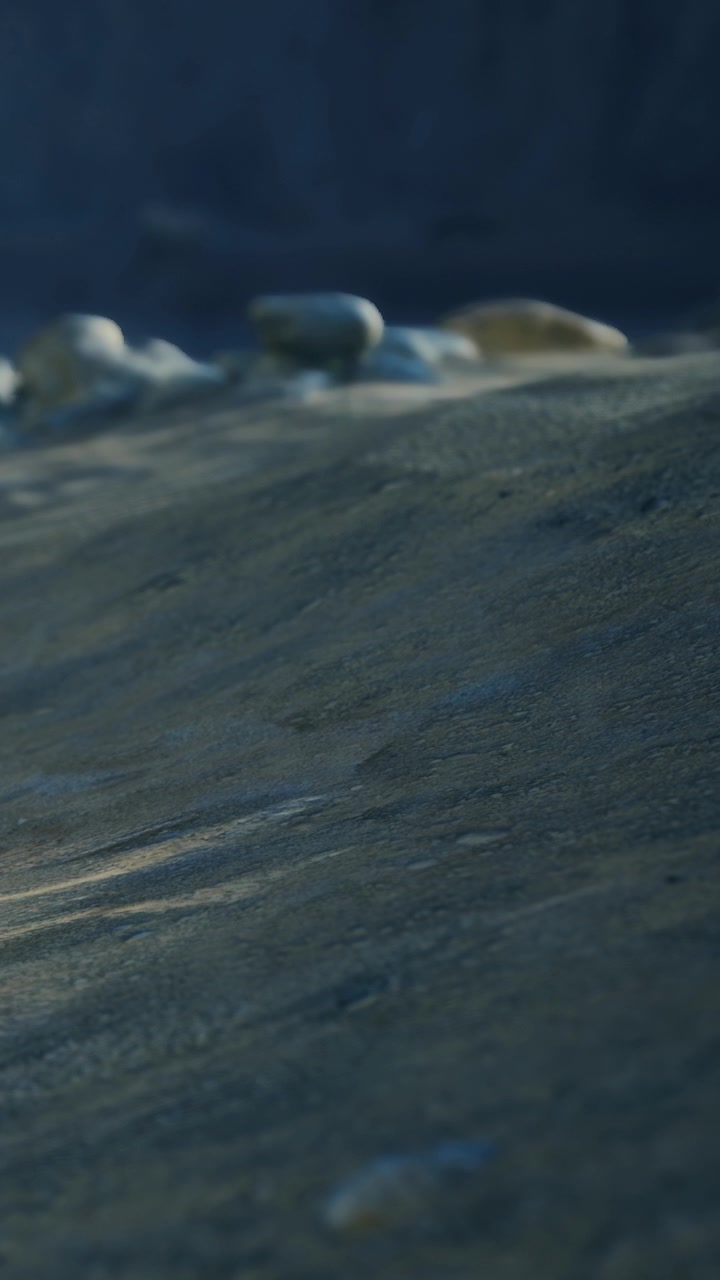 Waves move sand on a beach during low tide in summer sunlight