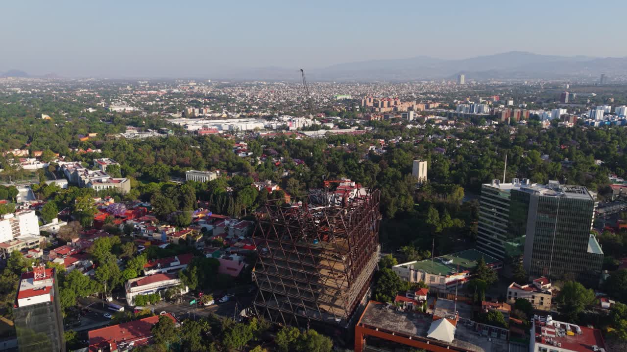 Aerial orbital shot of a high-rise under construction with cranes and steel framework in CDMX