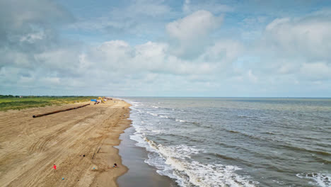 experience the stunning synergy of a sandy beach and the gentle crash of waves along the coastline through an aerial drone