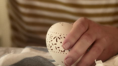 hand carefully decorates ornate pattern on easter madeira egg, close-up