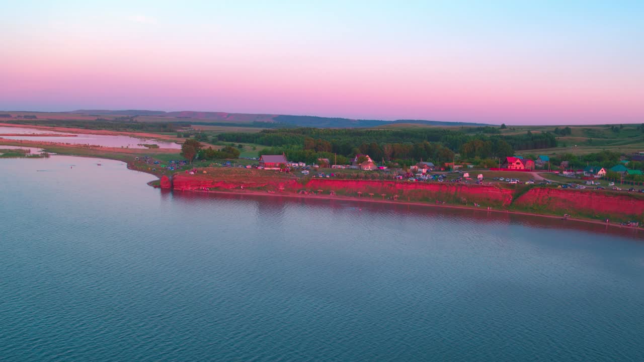 마을은 초록색 잔디로 인 언덕에 위치하고 있습니다. 분홍색 하늘, 배경에 해가 지는. 휴양지, 산책하기위한 그림 같은 장소. 자연 풍경.
