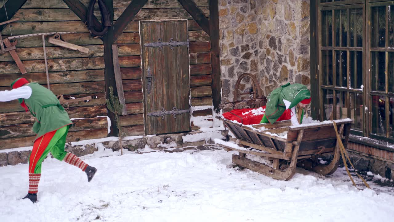 Couple of elves are playing snowballs running around a backyard. Holidays. Christmas eve. New year is coming. Having winter fun. Boy and a girl wear elves suits, costumes.