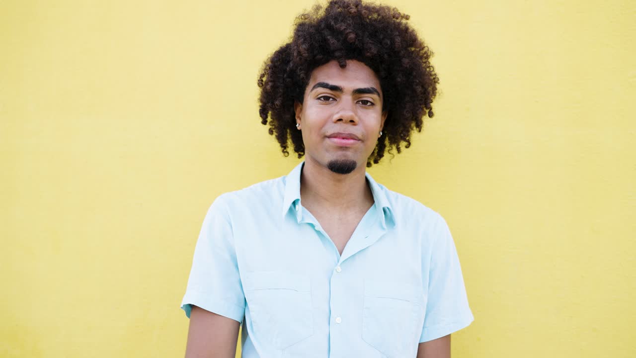 Man with curly hair giving thumbs up against yellow background