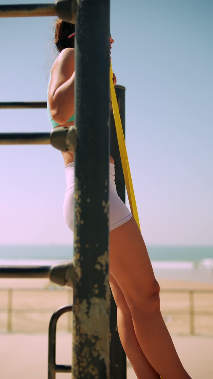 Fit Woman Doing Assisted Pull-Ups with Resistance Band at Outdoor Beach Gym