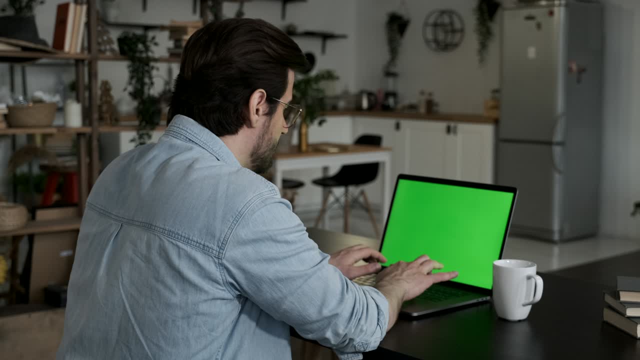 sobre el hombro del hombre trabajando en línea en una computadora portátil con pantalla verde en el espacio de vida