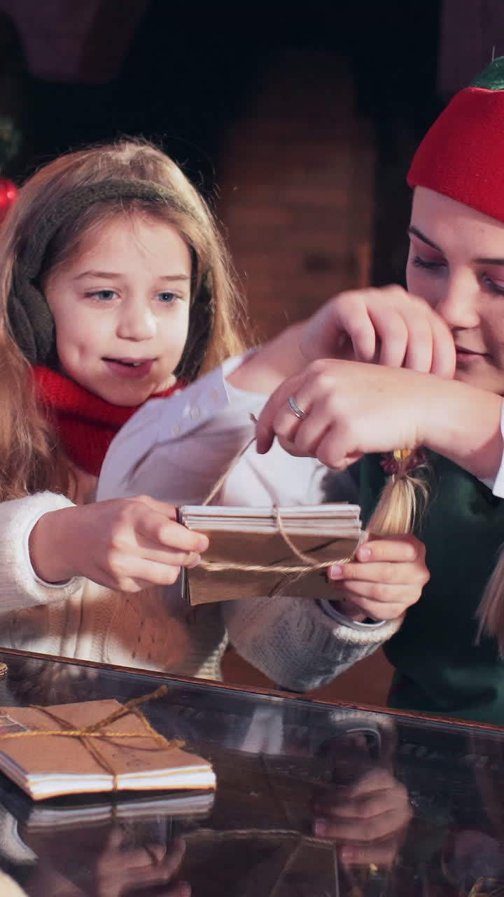 Girl with Santa Claus elf bandit letters to children in a room with a fireplace and a Christmas tree. Vertical video