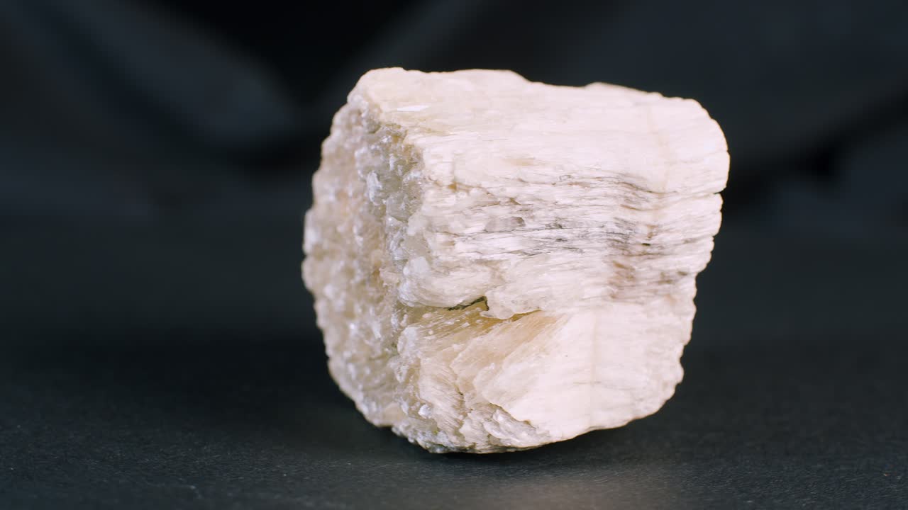 Kousek minerálu selenit na černém pozadí, rotující pohled
