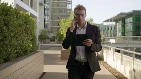 man walking outside, talking on phone, looking at tablet