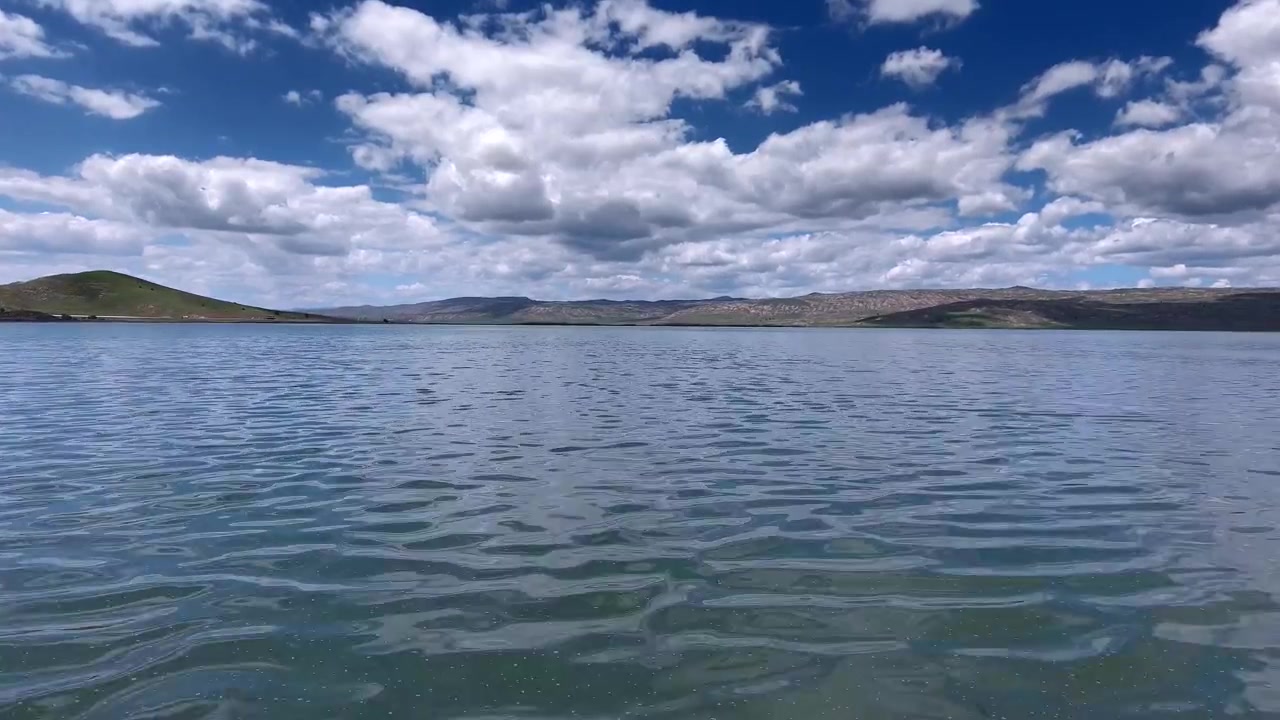 Paisaje sereno de lago con colinas ondulantes y cielo azul nublado