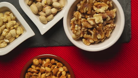 close up overhead shot of bowls containing cashews dry roasted peanuts pistachio walnuts and hazelnut nuts revolving 1