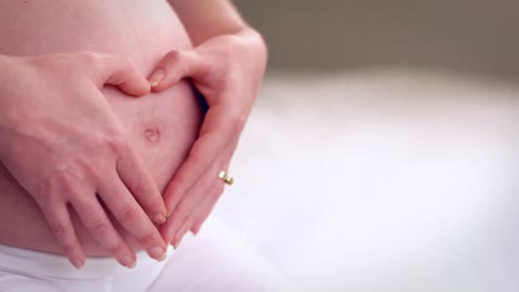 pregnant woman putting hands on belly making heart