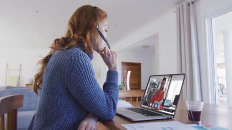 mujer de negocios caucásica sentada en un escritorio usando una computadora portátil haciendo una videollamada con una colega