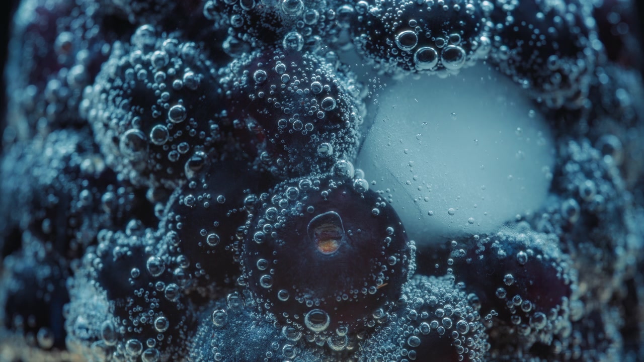 Macro primo piano di mirtilli e cubetti di ghiaccio in acqua frizzante con bolle d'aria.