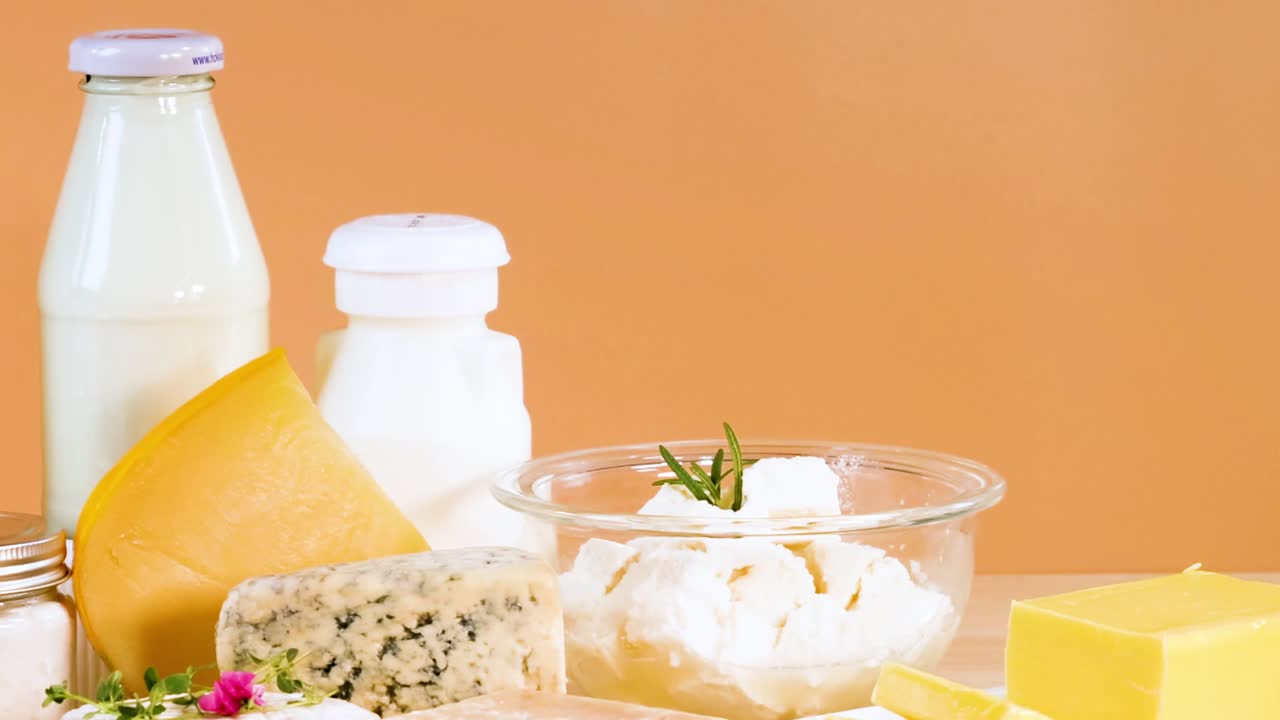 A selection of dairy items including milk, cheese, and yogurt jars against an orange backdrop.