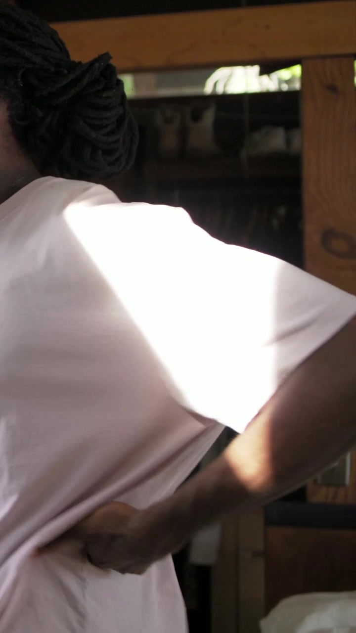Video verticale: La luce del sole colpisce un uomo in maglietta rosa che si strofina la schiena per alleviare il dolore ed esce dall'armadio.
