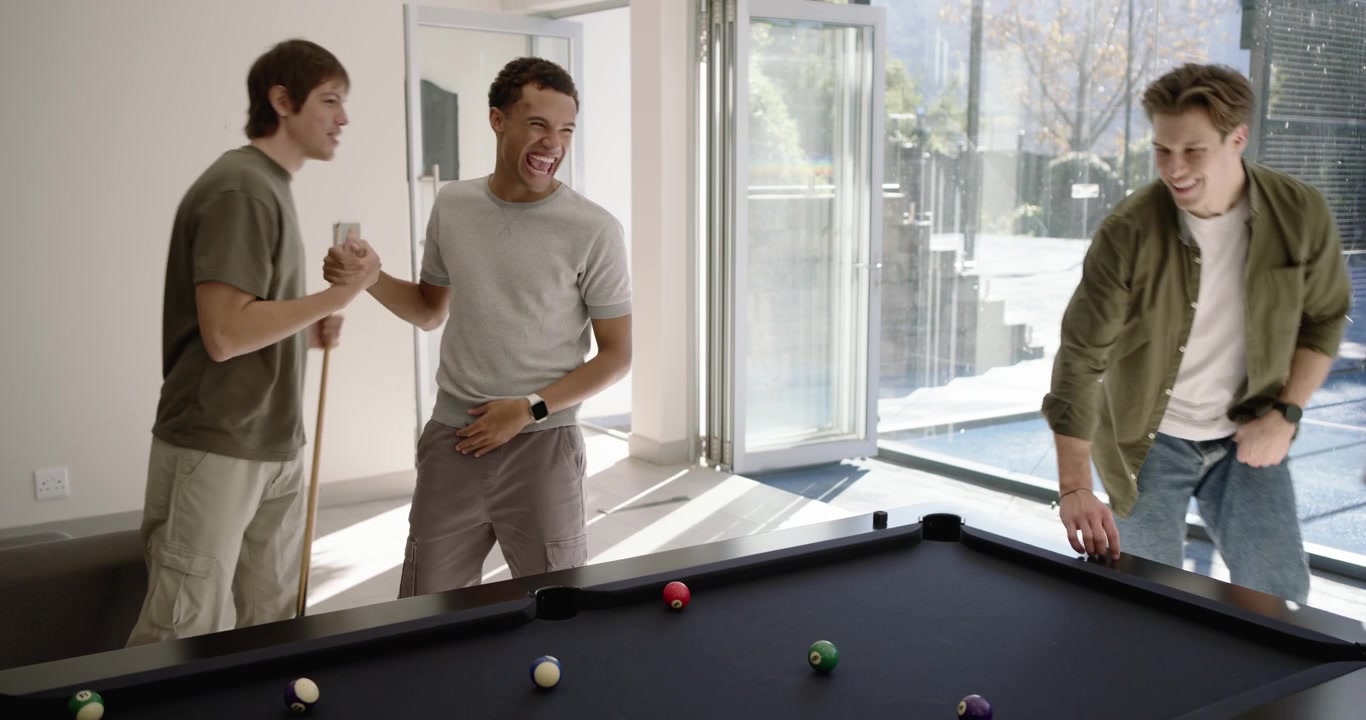 Men playing at pool table at home watching gesturing, shooter hitting cue ball, balls scattering
