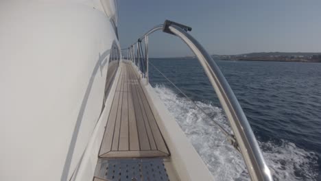 view down the side of a yacht of the narrow path on deck and the wake of the boat as it speeds through the water