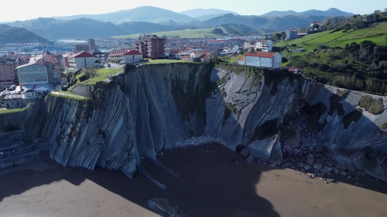 스페인 주마이아 (zumaia) 아래의 모래 해변에서 가파른 바위 조각 절벽이 형성됩니다.
