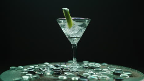 vaso de martini giratorio con una rodaja de limón y bloques de hielo, girando sobre una hermosa meseta con piedras brillantes, disparado sobre un fondo negro infinito
