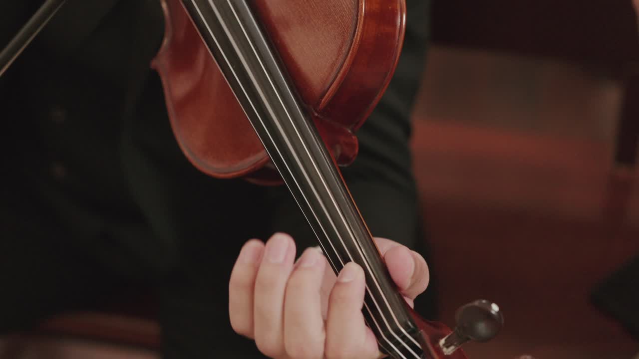 close up of violinist's hand pressing strings during indoor classical performance