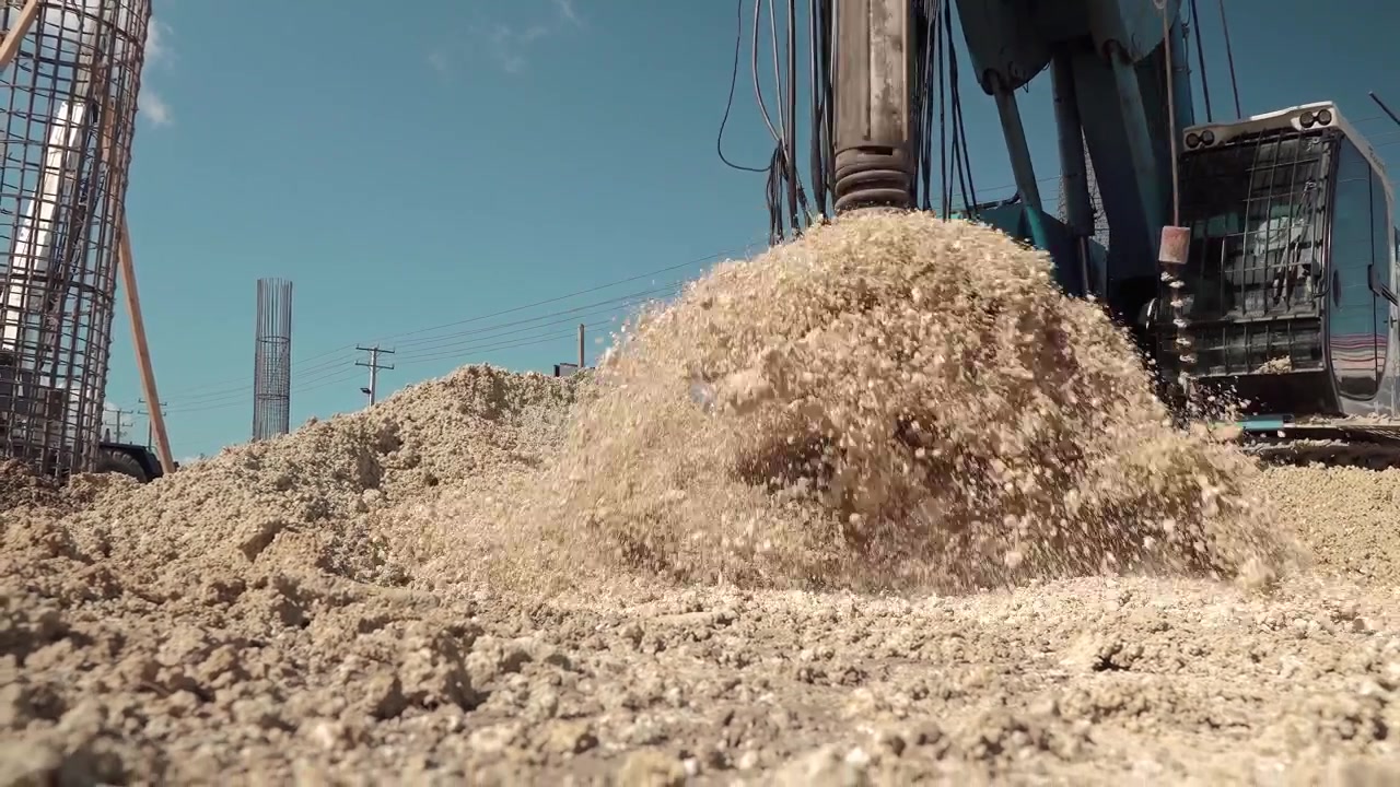 Toma estática a nivel del suelo y en ángulo bajo de un taladro de barrena de una perforadora hidráulica de pilotes girando rápidamente para descargar tierra sobre un montón de tierra en un sitio de construcción de ingeniería civil.