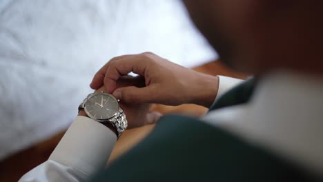 close up of groom adjusting silver wristwatch while wearing a formal suit before wedding