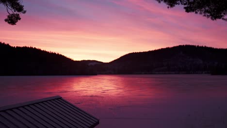 colorful pink sunset reflecting on frozen lake with silhouette mountain in norway