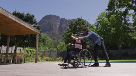 happy biracial woman in wheelchair dancing in garden with smiling male partner with dreadlocks