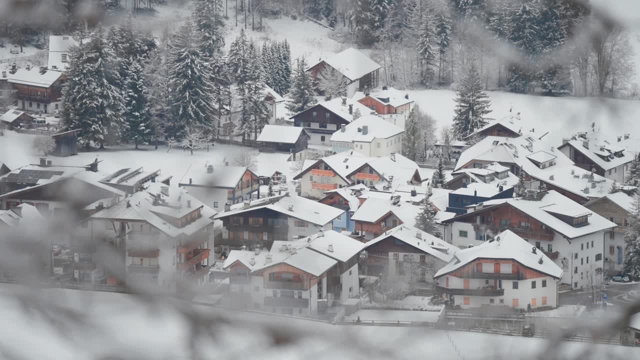 A charming Alpine village blanketed in snow sits peacefully at the edge of a pine forest in the Dolomites.