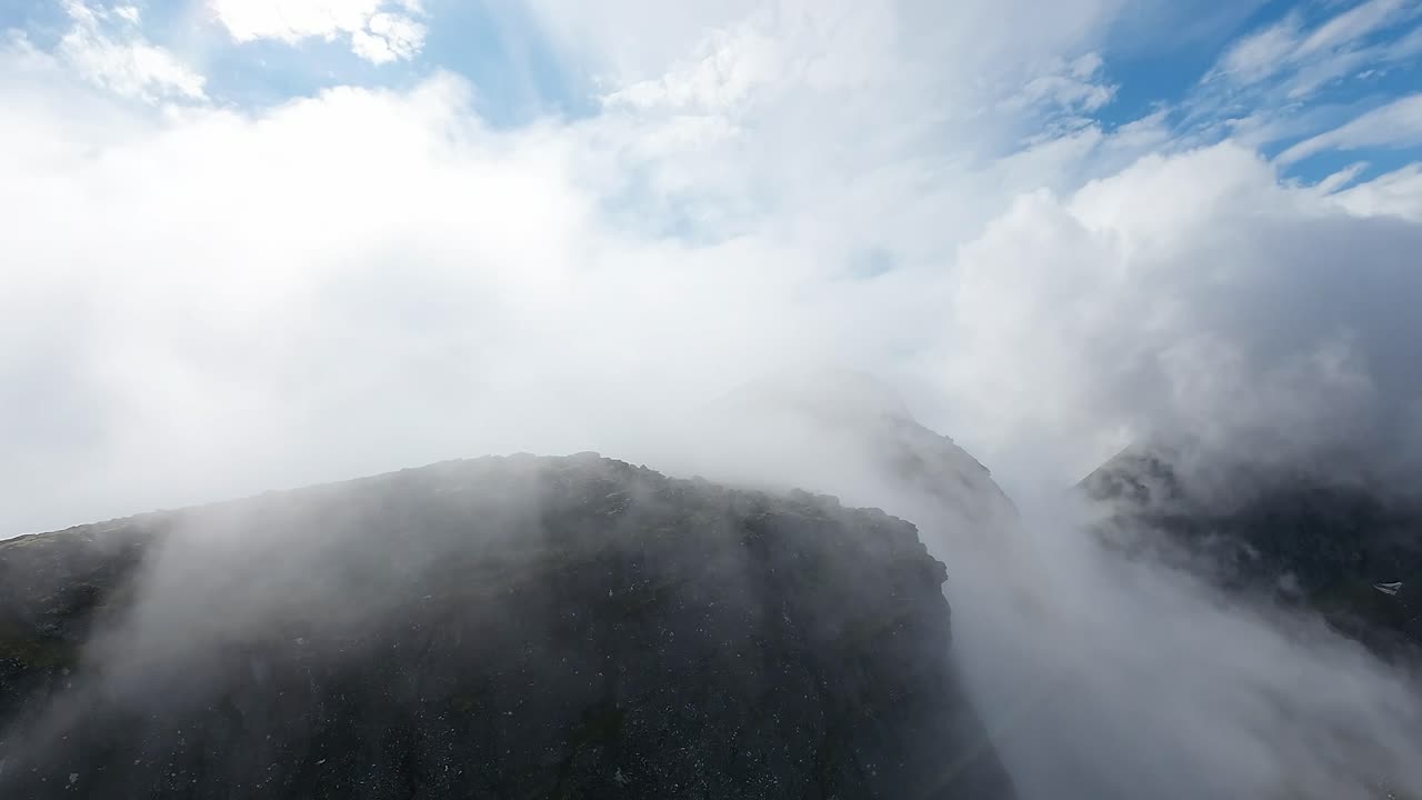 FPV drone takes a daring dive through mist down a colossal mountain's sheer vertical face, capturing a surreal descent through the clouds