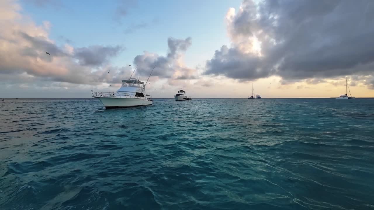 View from boat sailing the Caribbean Sea at sunset with fishing boats and yatchs on calm turquoise water
